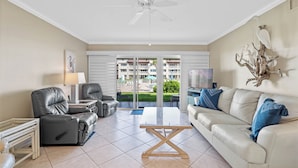 A living room with a sofa, two recliners, a coffee table, and a ceiling fan. - Chateau by the Sea 13A Pure Ocean Bliss! (New Smyrna Beach)
