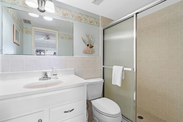 Een badkamer met een wit wastafel, spiegel en toilet. Er is een douche met een glazen deur en een handdoek hangt aan de muur.