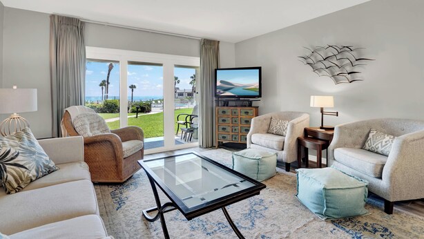 A spacious living room with a glass coffee table, two sofas, and a television.