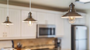 A kitchen with white cabinets, a stainless steel microwave, and a refrigerator. - Chateau by the Sea 25C Serenity by the Sea (New Smyrna Beach)