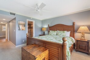 Ein Schlafzimmer mit einem hölzernen Bett, einem Nachttisch mit Lampe, einem Deckenventilator und einer Tür zu einem anderen Raum.