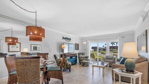 A spacious living area with wicker furniture, a dining table, and a view of the outdoors. - Chateau by the Sea 12D Ocean Breeze & Views! (New Smyrna Beach)