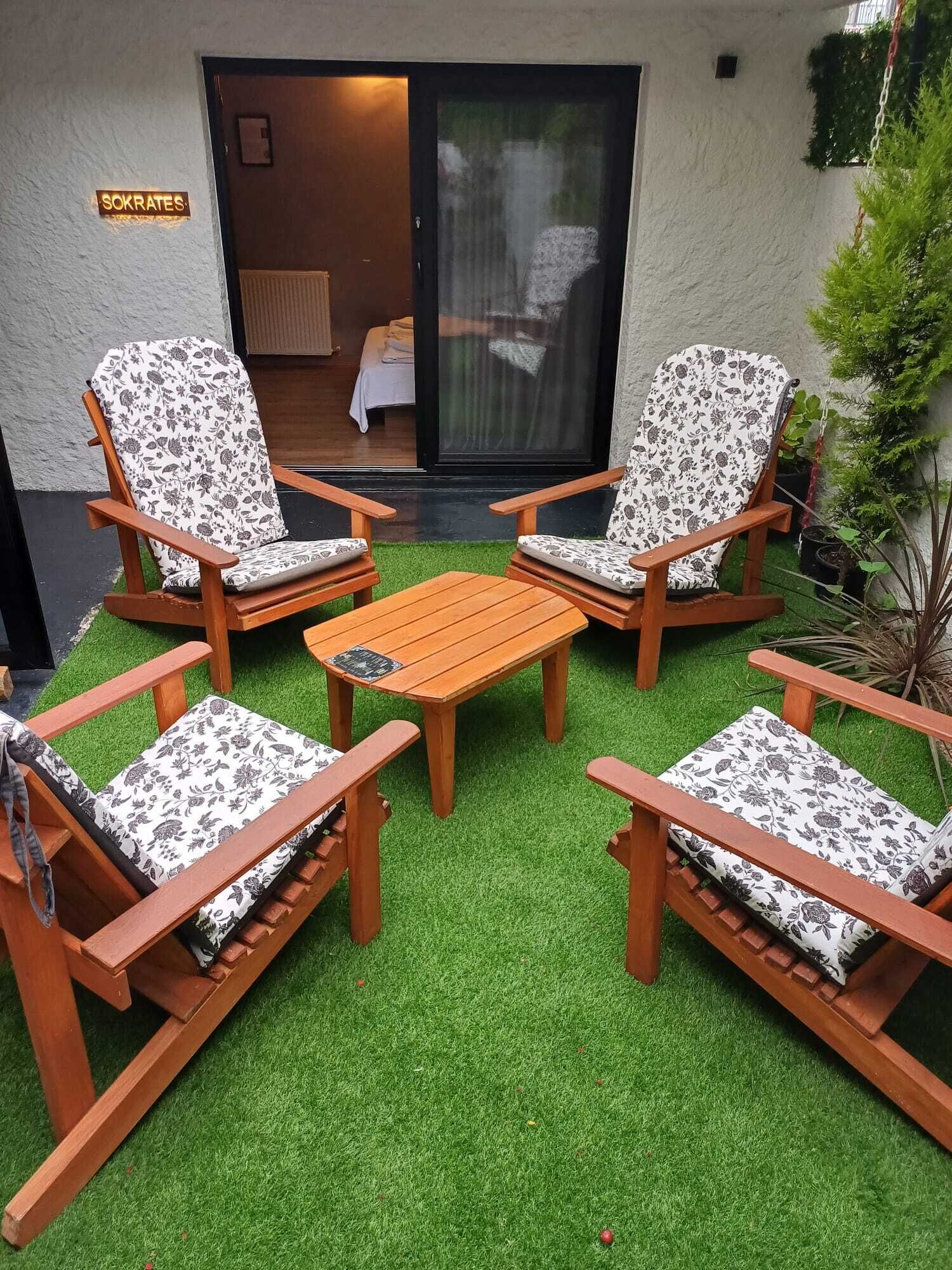 A patio with four wooden chairs and a table, surrounded by artificial grass.