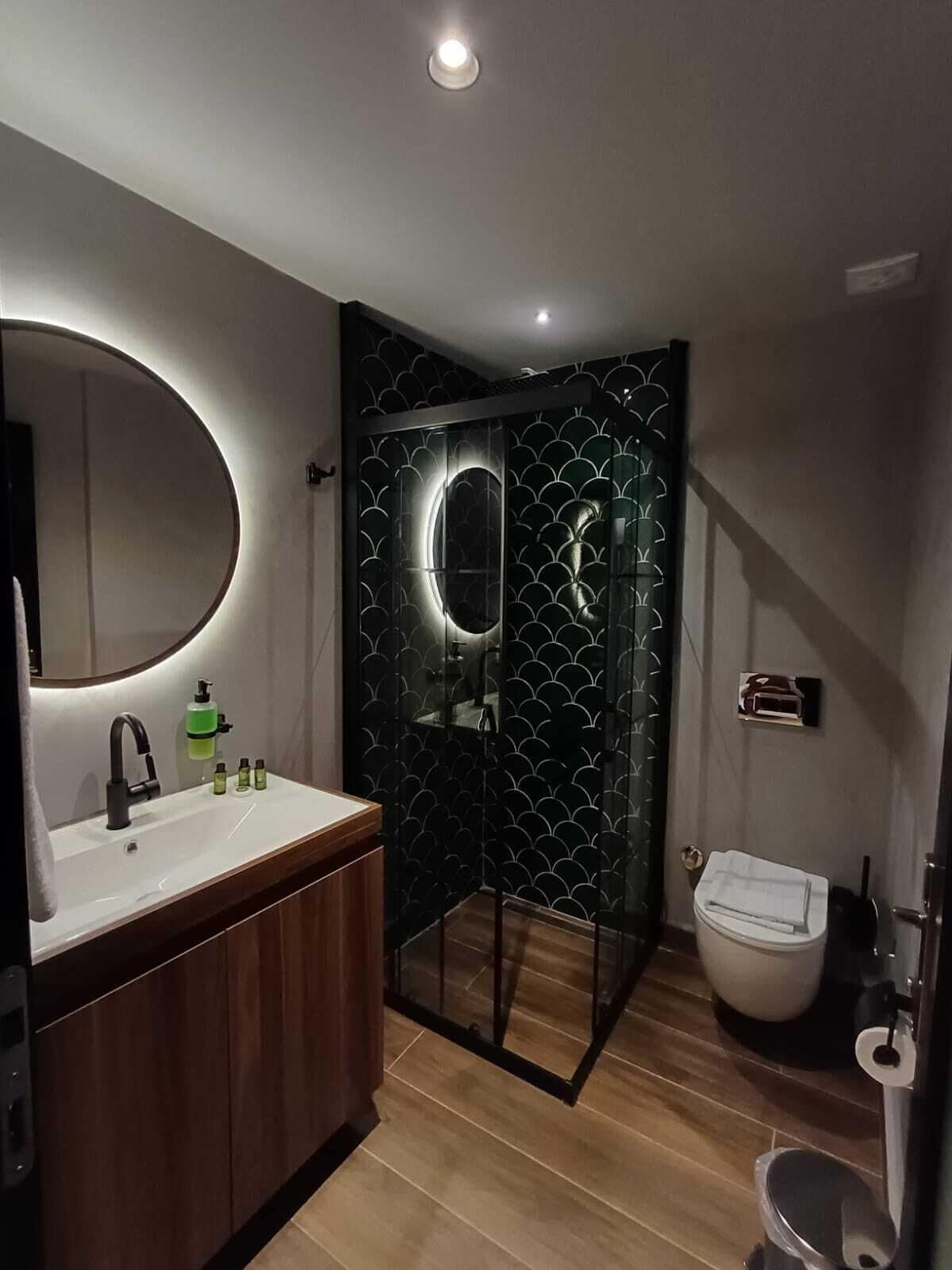 A modern bathroom with a wooden vanity, a round mirror, and a glass-enclosed shower.