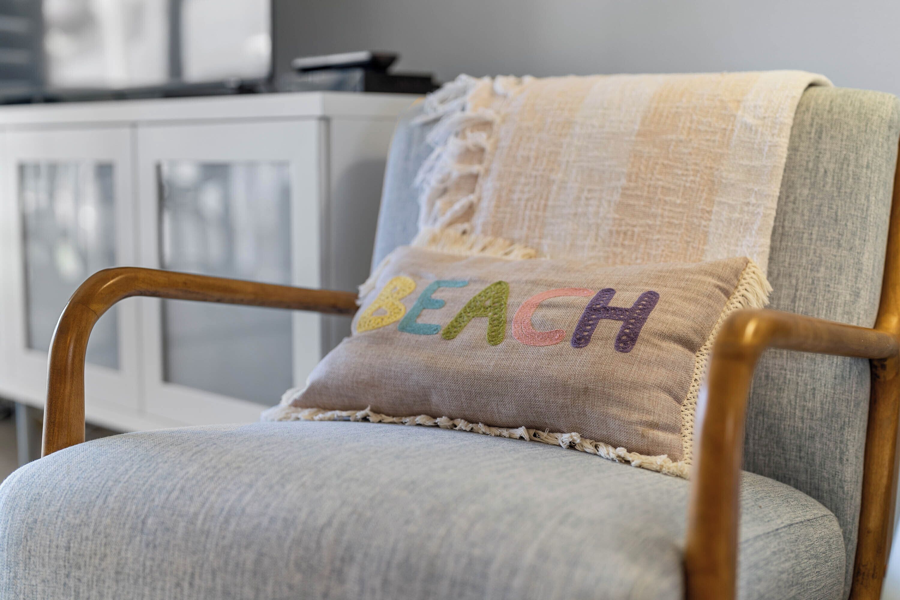 Une chaise avec un coussin orné d’une broderie représentant le mot « PLAGE ».