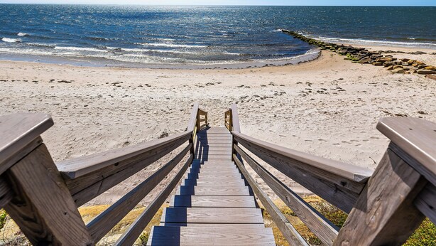 A wooden staircase leading to a sandy beach with a view of the ocean. - Recently updated home sleeping 10, steps to the beach! (Harwich Port)