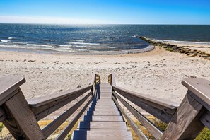 Un escalier en bois mène à une plage de sable fin, d’où l’on a une vue sur l’océan.