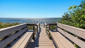 A wooden boardwalk leading to a beach with clear blue water and a distant shoreline. - Recently updated home sleeping 10, steps to the beach! (Harwich Port)