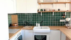 Kompakti keittiö, jossa on valkoiset kaapit, vihreät laatat seinän suojapintana, puinen työtaso ja sisäänrakennettu uuni.