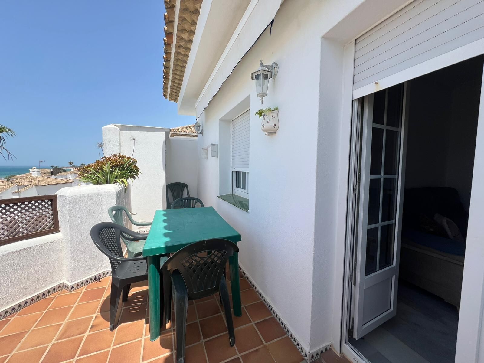 Un balcón con una mesa y sillas, una planta en maceta y vista al mar.
