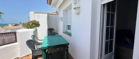 Un balcón con una mesa y sillas, una planta en maceta y vista al mar.