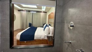 Una habitación de hotel moderna con un espejo grande, una cama bien hecha, una mesita de noche y un baño con ducha e inodoro.