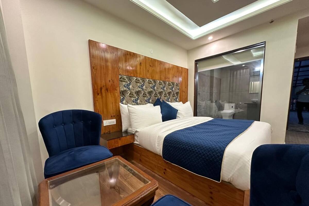 A hotel room with a wooden headboard, two beds with blue and white bedding, a glass coffee table, and a blue armchair.