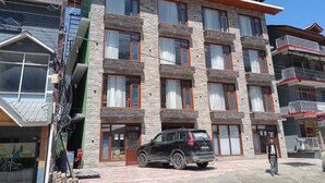 Un edificio de varios pisos con fachada de piedra, varios balcones y un SUV negro estacionado frente a él.