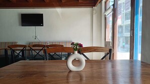 Un salón de conferencias con una mesa de madera, sillas, un jarrón blanco con flores y un televisor en la pared.