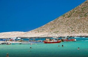 Una playa con barcos y gente nadando.