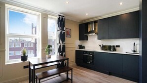 A modern kitchen with dark cabinetry, a built-in oven, and a window with a view of buildings. - The Balham Hideout - Trendy 2bdr Flat (London)