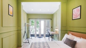 A hotel room with a bed, a desk, and a chair, a large window, and a door leading to an outdoor area. - The Balham Place - Stylish 2bdr Flat (London)