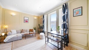 A modern living room with a sofa, coffee table, and dining table. There are potted plants and artwork on the walls. - The Balham Place - Stylish 2bdr Flat (London)