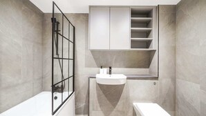 A modern bathroom with a bathtub, toilet, and built-in vanity with shelves. - The Balham Place - Stylish 2bdr Flat (London)