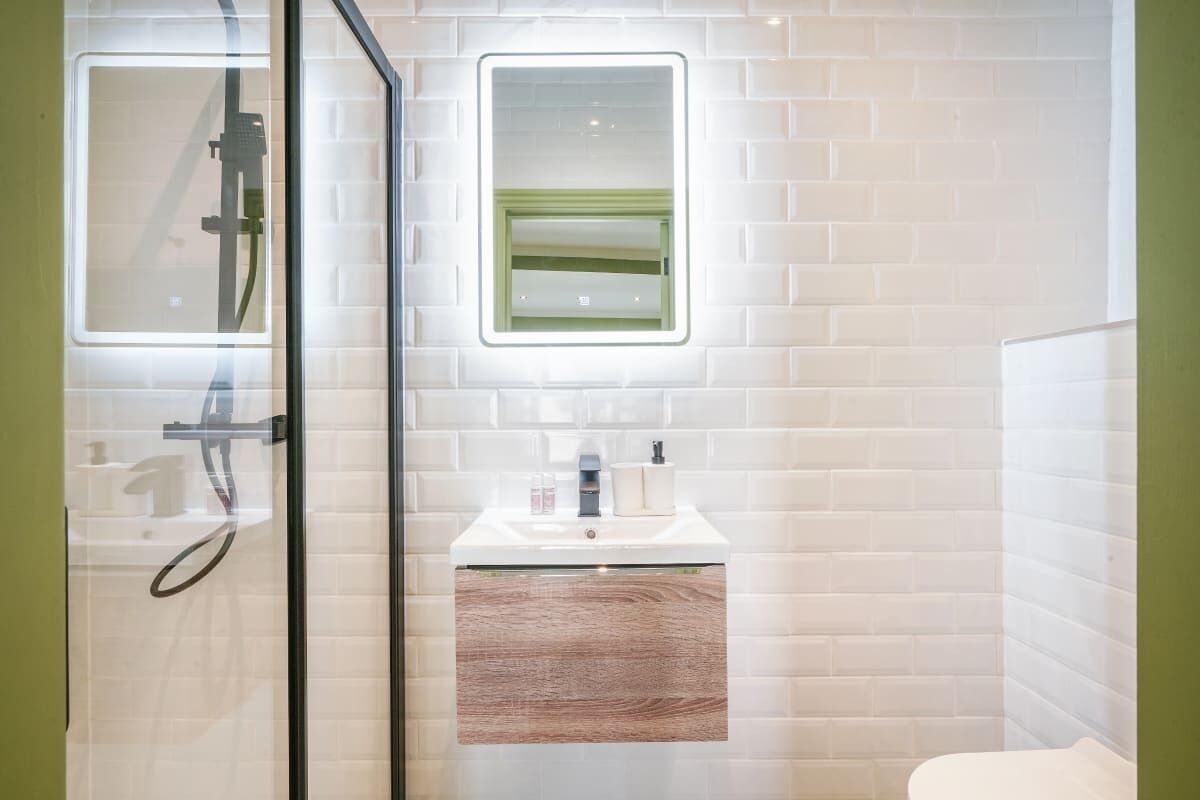 A modern bathroom with a glass shower enclosure, a white sink with a wooden vanity, and a small mirror above the sink.