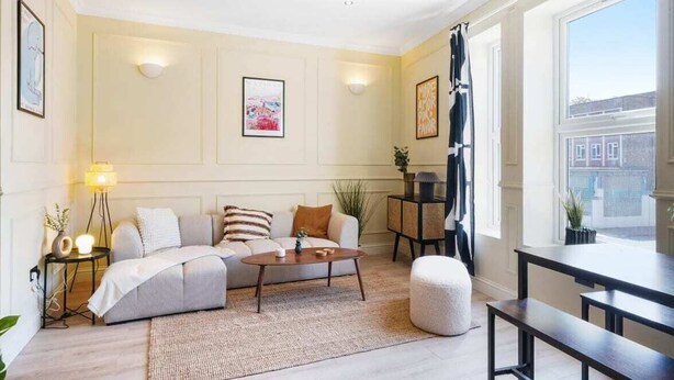 A modern living room with a sofa, coffee table, and a dining area with benches. - The Balham Place - Stylish 2bdr Flat (London)
