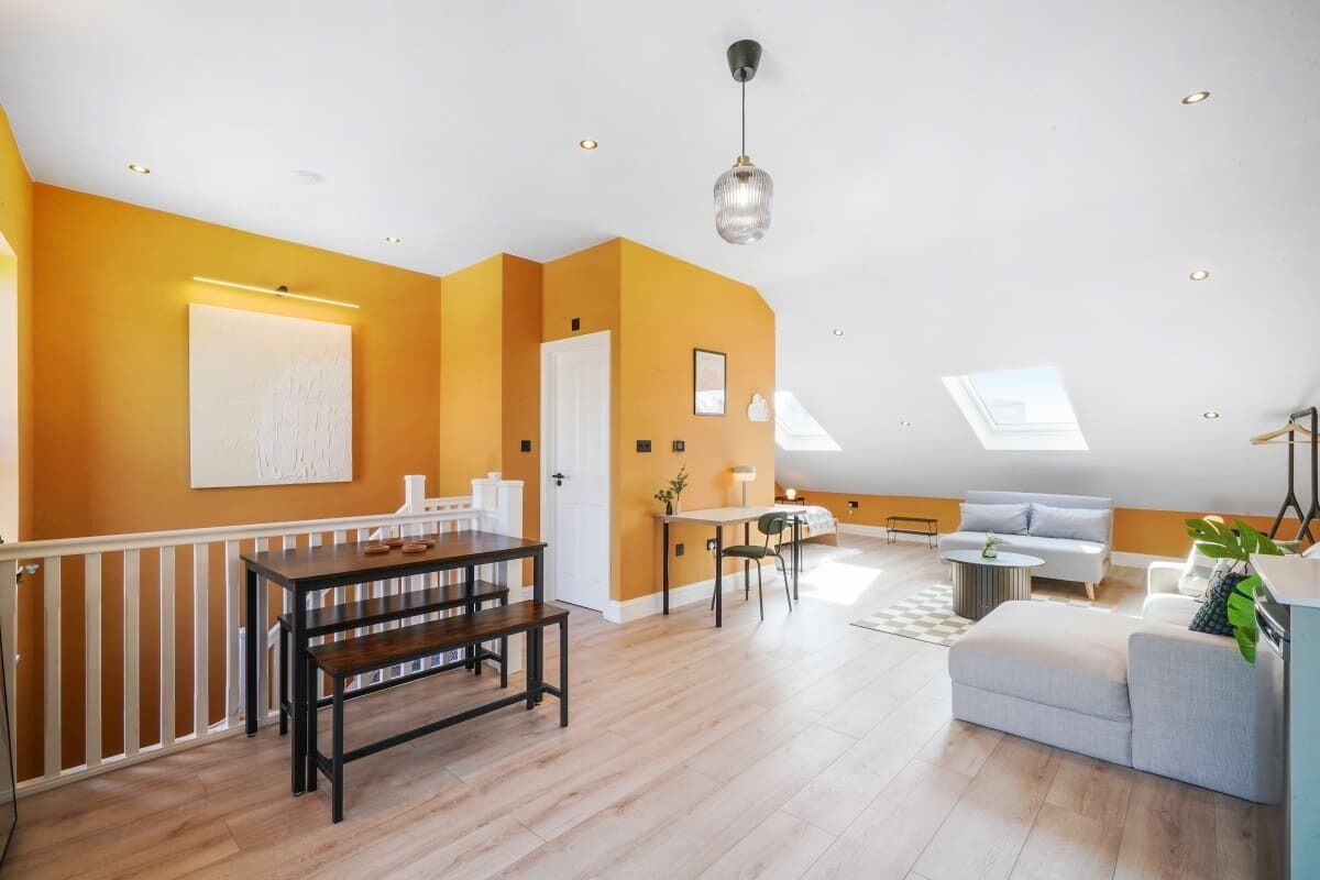 A spacious living area with a high ceiling, a dining table, a sofa, and a staircase leading to an upper level.