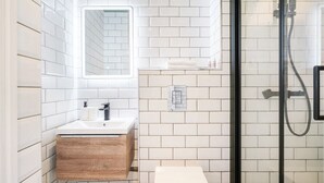 Une salle de bain moderne avec des carreaux de métro blancs, un meuble-lavabo en bois, un lavabo blanc, un miroir et une douche séparée par une paroi en verre.