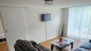 A modern living room with two black sofas, a glass coffee table, and a flat-screen TV mounted on the wall. - Luxury Apartment Garden (Brienz)