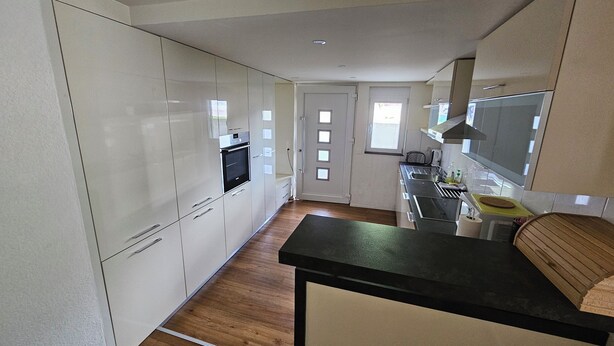 A kitchen with white cabinets, a black countertop, and a wooden floor. - Luxury Apartment Garden (Brienz)