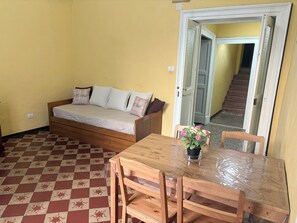 A room with a sofa bed, a wooden dining table with chairs, and a staircase leading to an upper floor. - House Benedettini's a Catania Centro tra il Monastero dei Benedettini e il Duomo (Catania)
