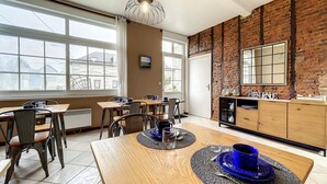 A dining area with a brick wall, large windows, and a wooden table set for two. - 2 Bedroom Bed & breakfast in Hucqueliers (Hucqueliers)