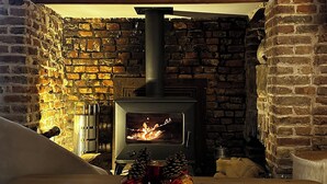 A cozy room with a brick wall, a wood-burning stove, and a table with a decorative item. - 2 Bedroom Bed & breakfast in Hucqueliers (Hucqueliers)
