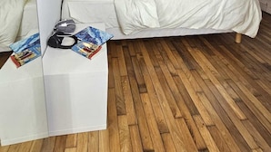 A modern bedroom with a bed, wooden flooring, a white bedside table, and a ceiling vent.