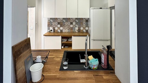 A compact kitchen with white cabinets, a tiled backsplash, and a built-in refrigerator.