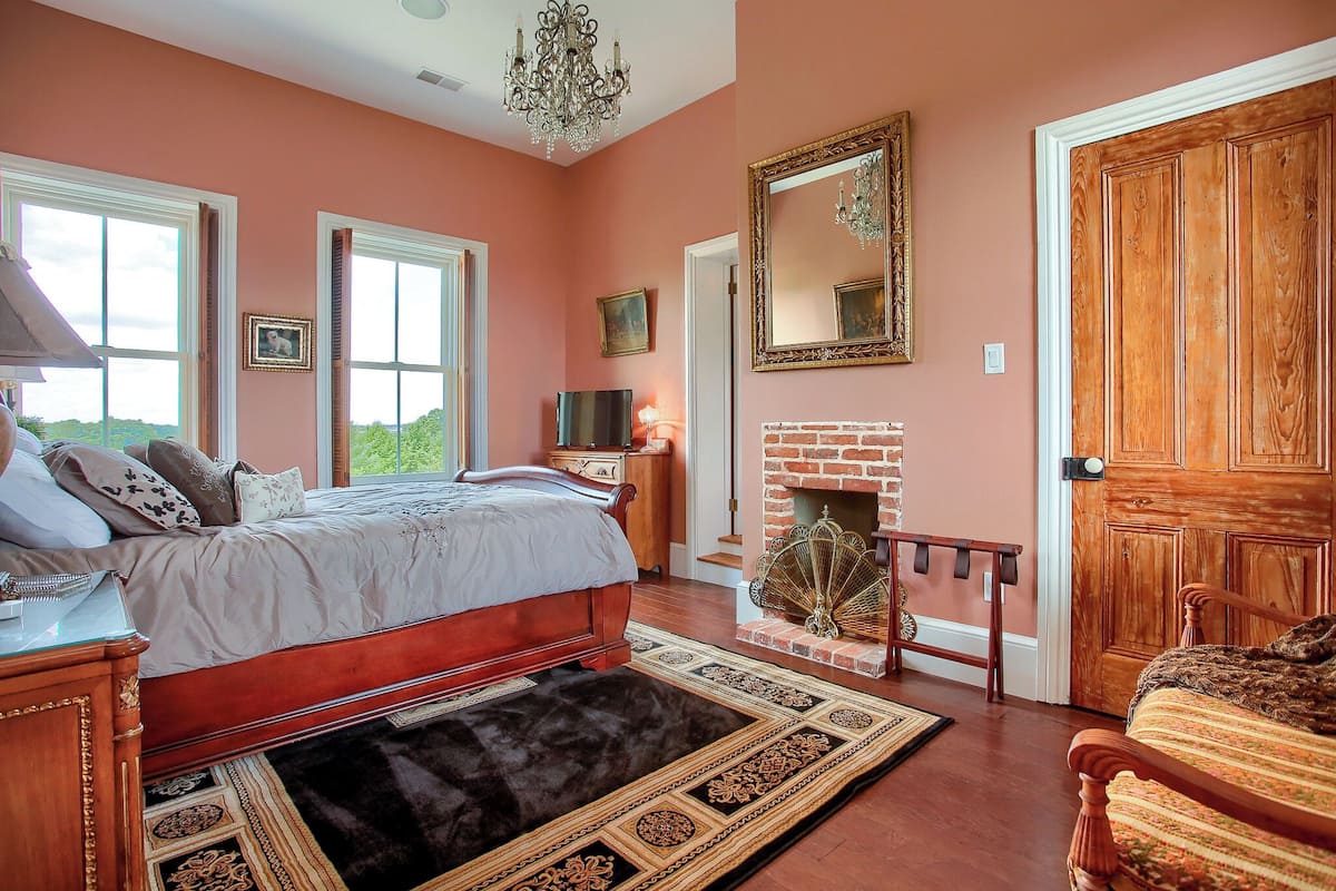 A bedroom with a large bed, a fireplace, and a wooden door.