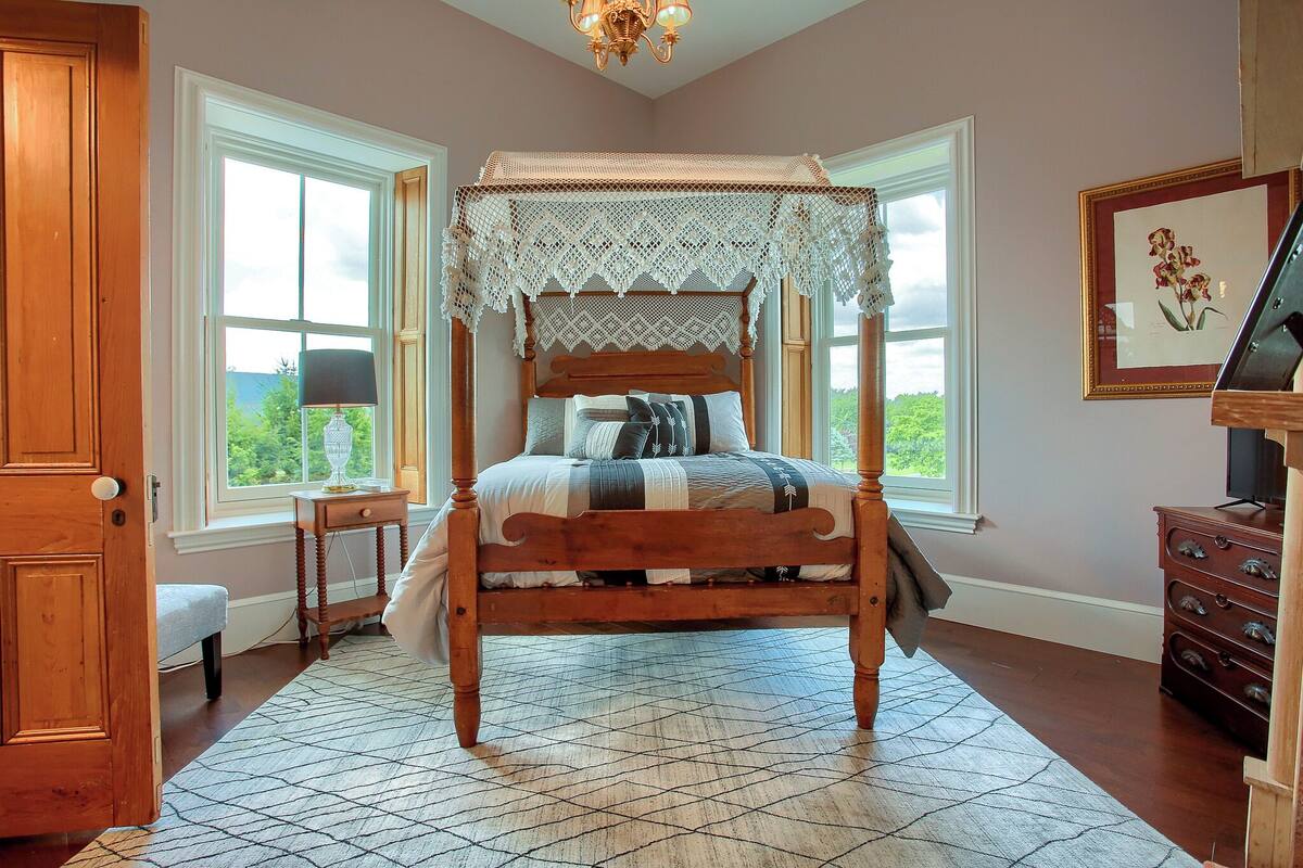A four-poster canopy bed with a lace headboard, a bench at the foot of the bed, and a dresser with drawers to the right.