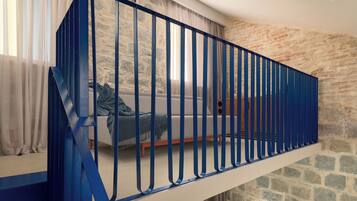 Une chambre de style loft moderne, avec un mur en pierre, une rambarde bleue et une grande fenêtre ornée de rideaux légers.