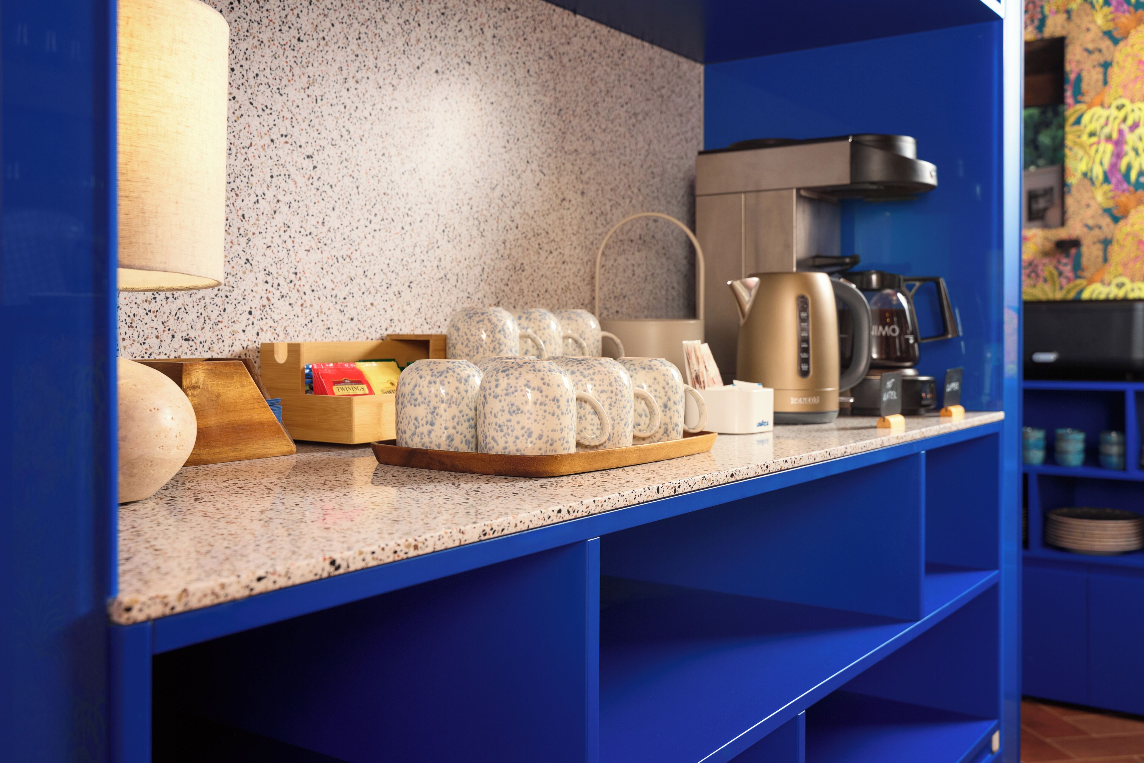 Una cocina con encimera de granito, armarios azules, cafetera y hervidor.