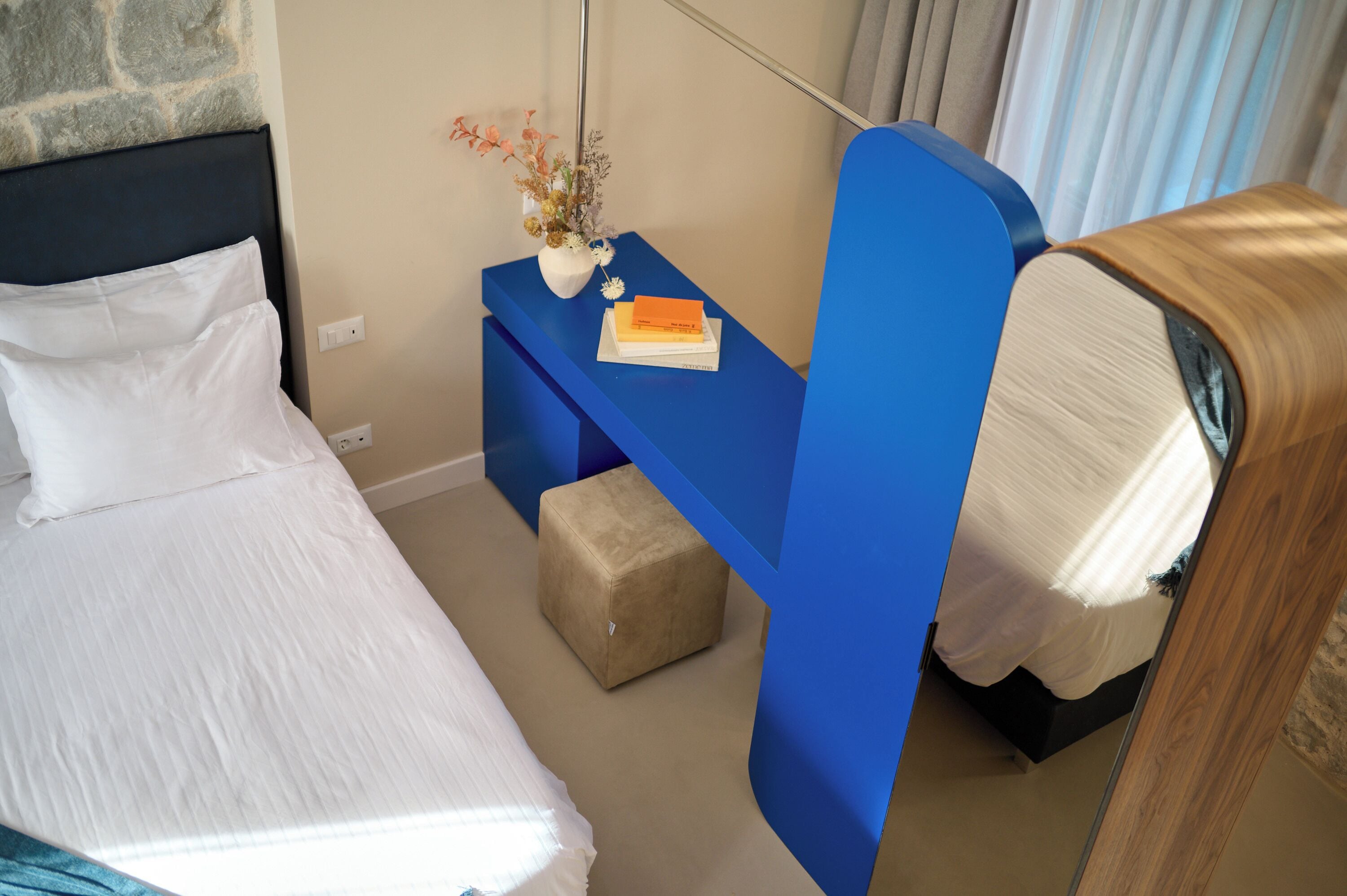 A hotel room with a bed, a blue nightstand with a vase of flowers, and a wooden headboard.