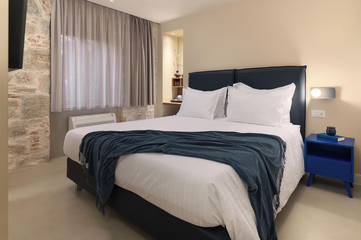 Un dormitorio moderno con una cama grande, una pared de acento de piedra, una mesita de noche con lámpara y un espejo.