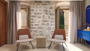 Una habitación con dos sillas, un pequeño reposapiés, una pared de piedra y un armario azul.