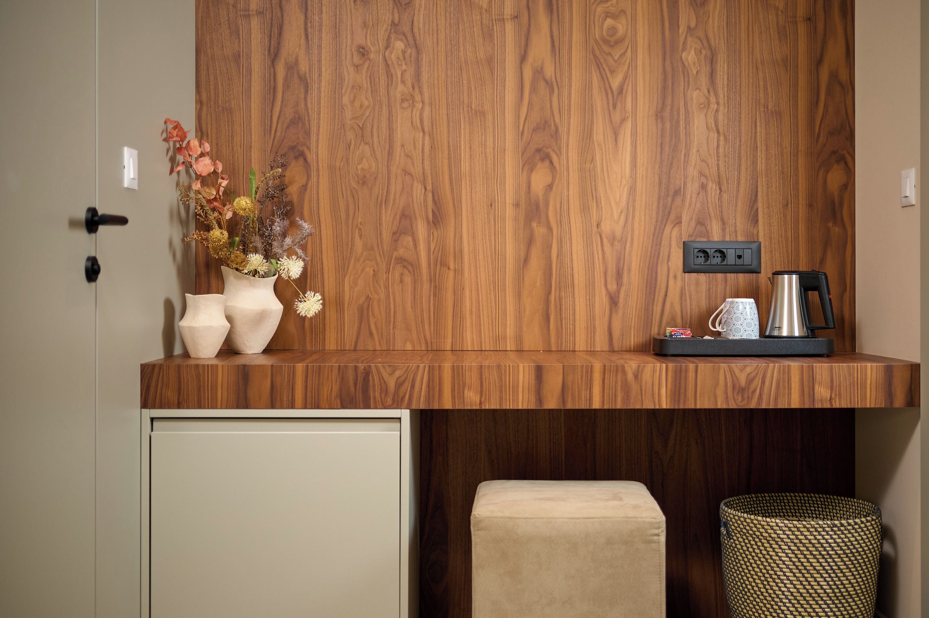 A wooden wall with a shelf holding a vase of flowers, a coffee maker, and a tray with a mug and a small item.