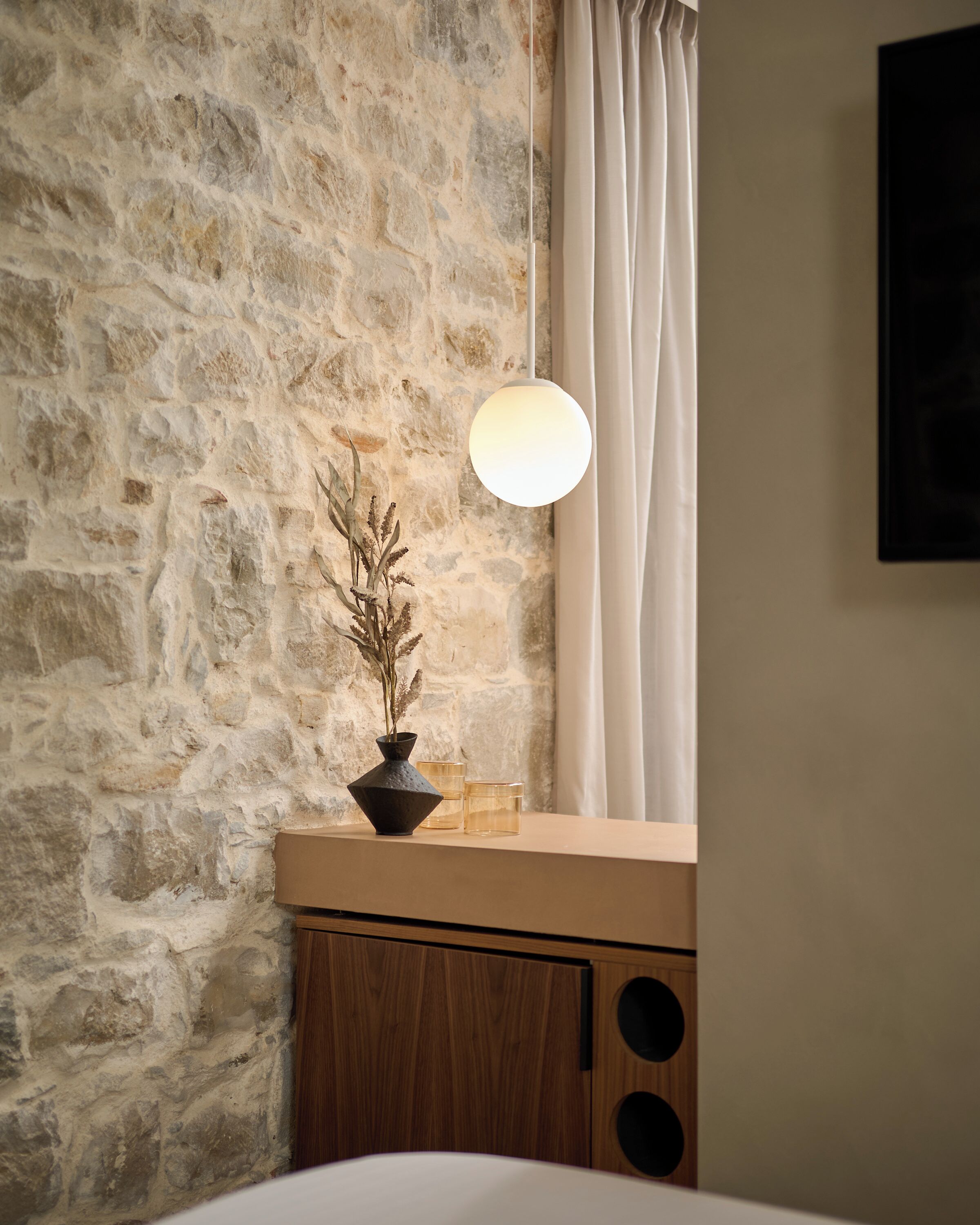 A stone wall, a wooden cabinet, a vase with dried plants, and a hanging light fixture.