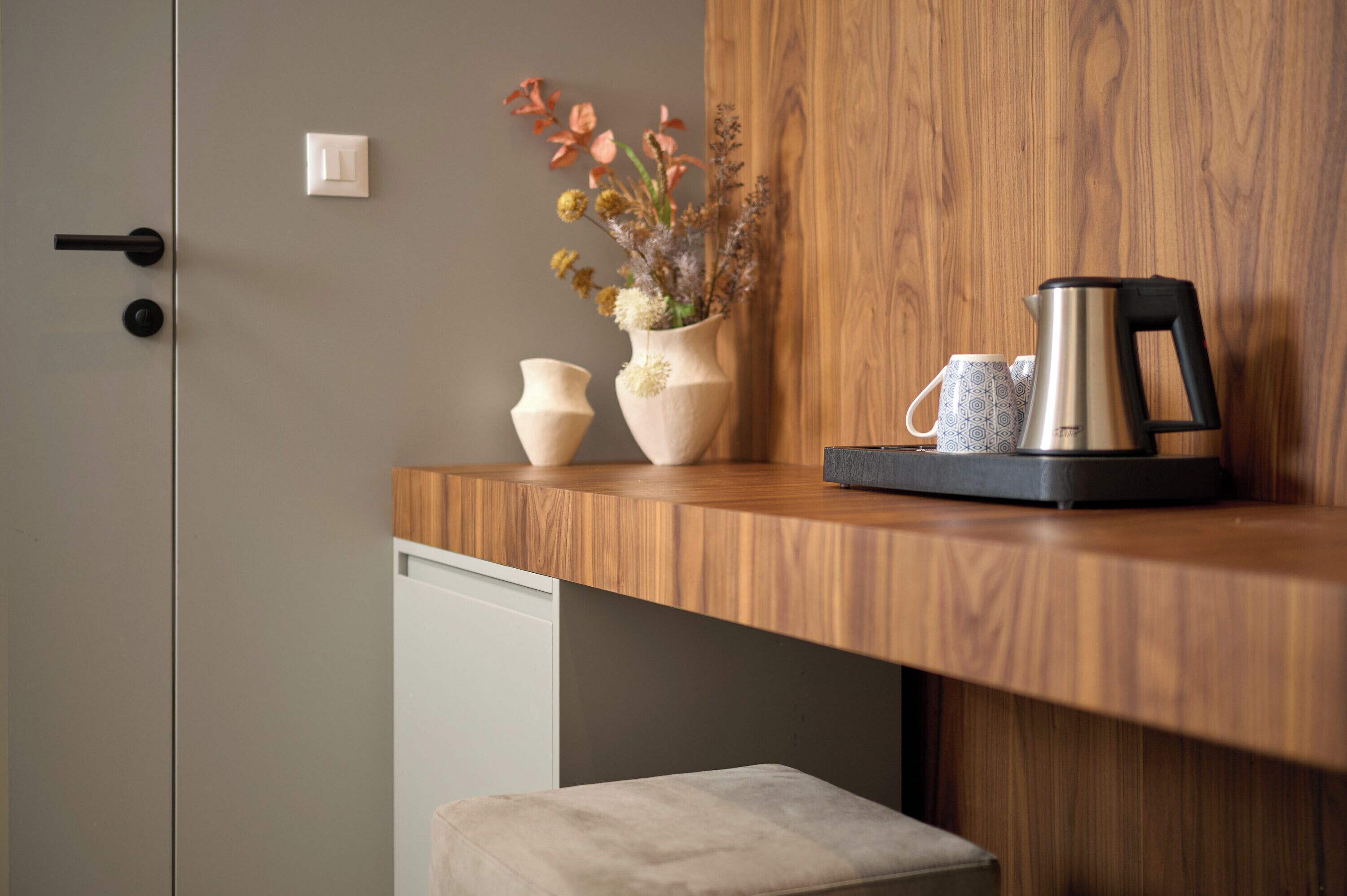 A kitchenette with a wooden countertop, a coffee maker, two vases with flowers, and a small white appliance.