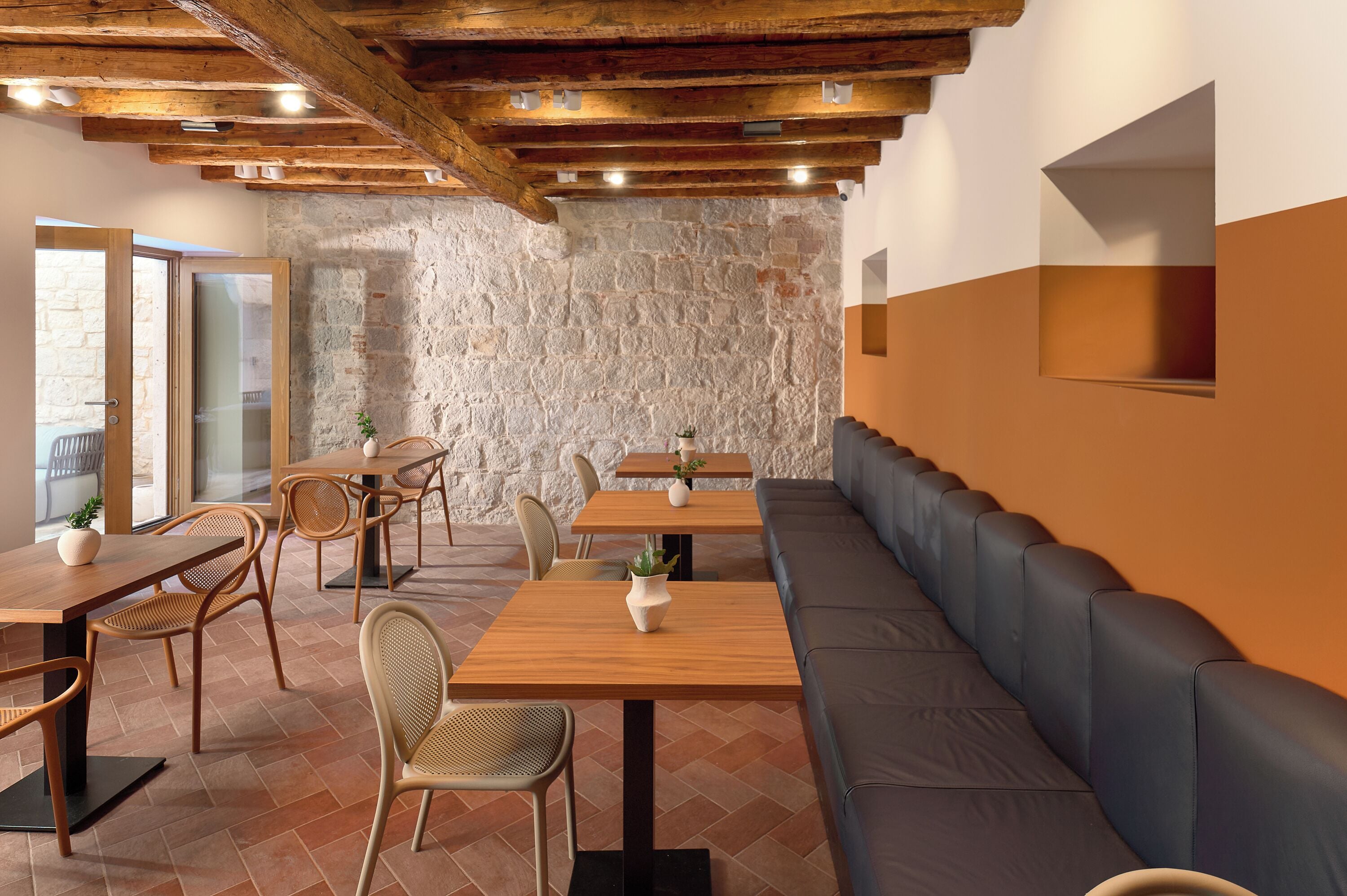 A restaurant with wooden tables and chairs, a stone wall, and a modern design.
