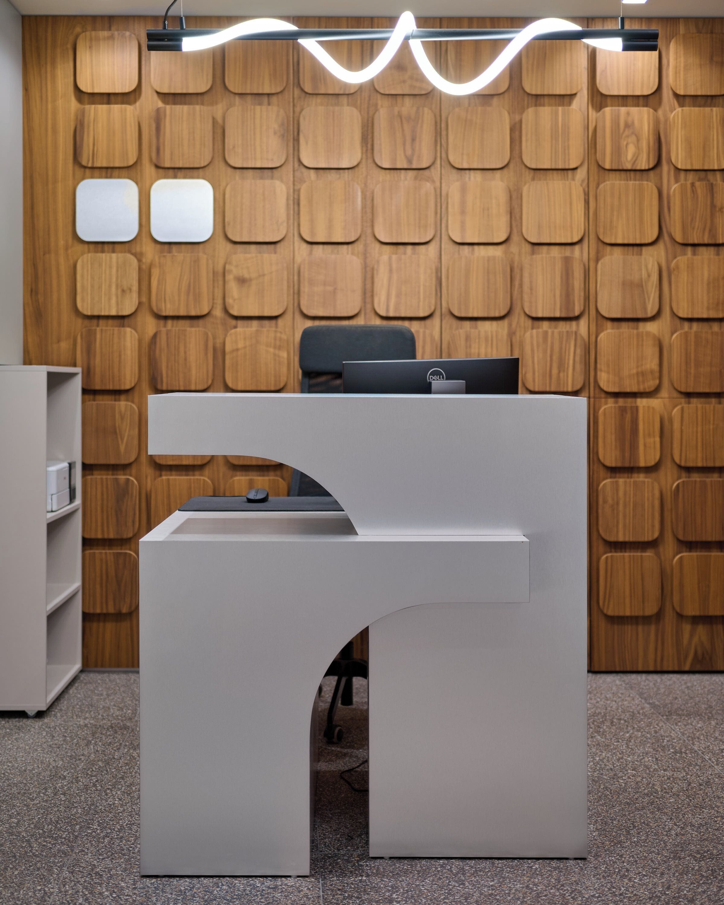 A modern office desk with a computer and a chair, set against a wooden wall with a unique pattern.