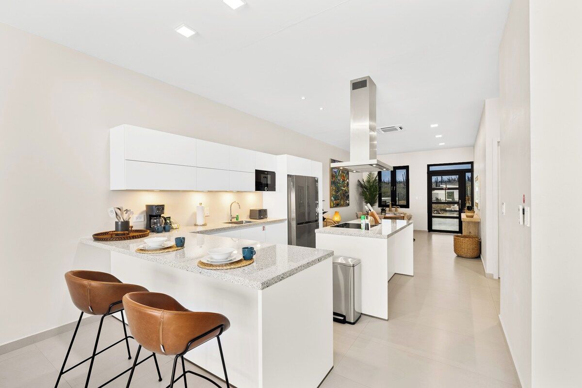 A modern kitchen with a central island, bar stools, and a stainless steel range hood.