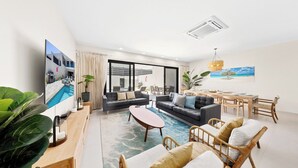 A modern living room with a flat-screen TV, sofas, a coffee table, and a dining area with chairs and a table. - Walk to Beach: 4BR Oasis w/ Pool, Spa, View (Noord)