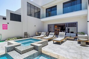 A modern outdoor pool area with tiered steps, lounge chairs, and a dining area.